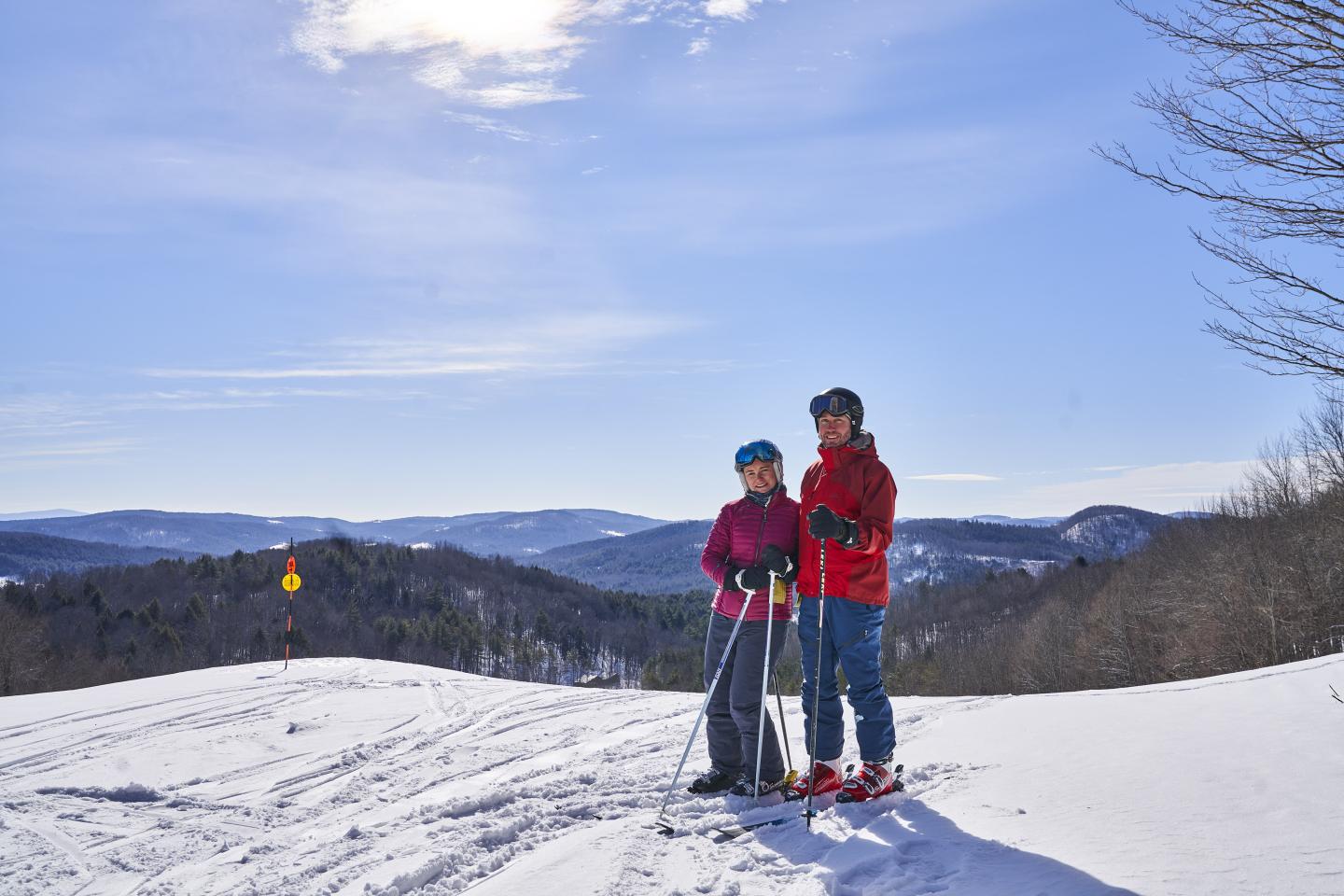 2 skiers stand in front of the view from the summit