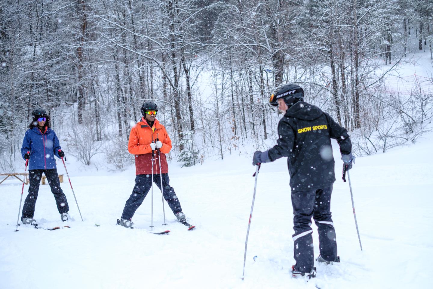 Ski instructor guiding two skiers on a snowy slope.