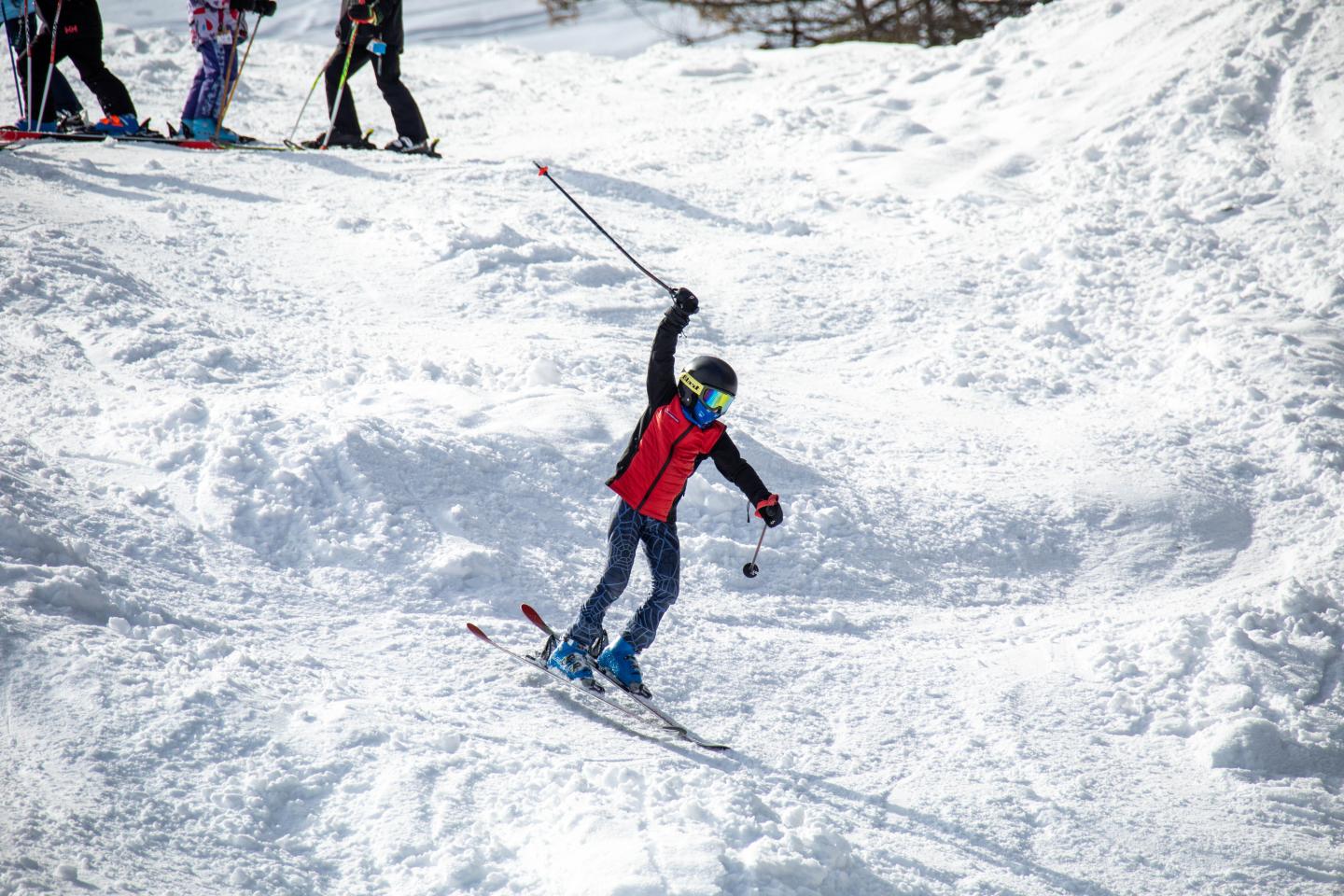 Skier in red jacket balancing on snowy slope.