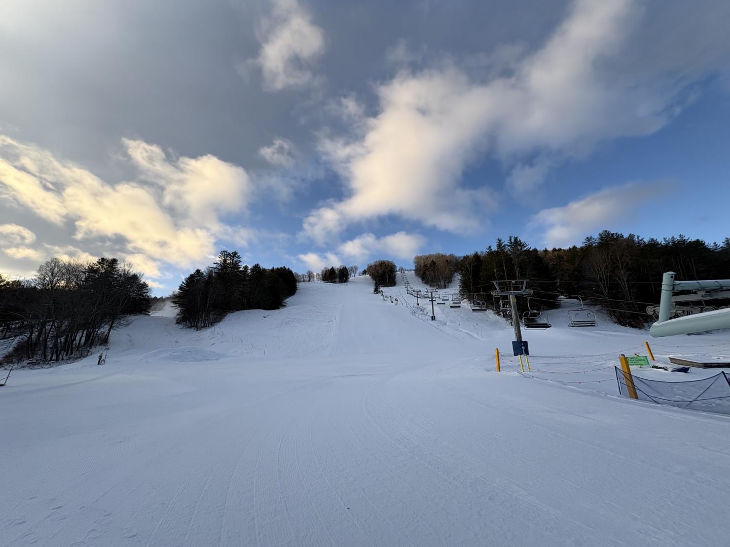 Snow-covered ski slope under a cloudy blue sky.