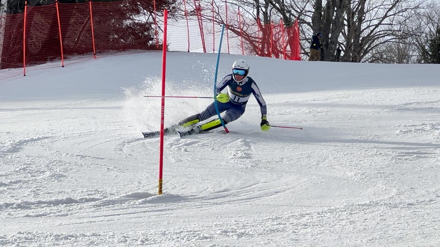 Skier in blue gear racing downhill past a red slalom gate.