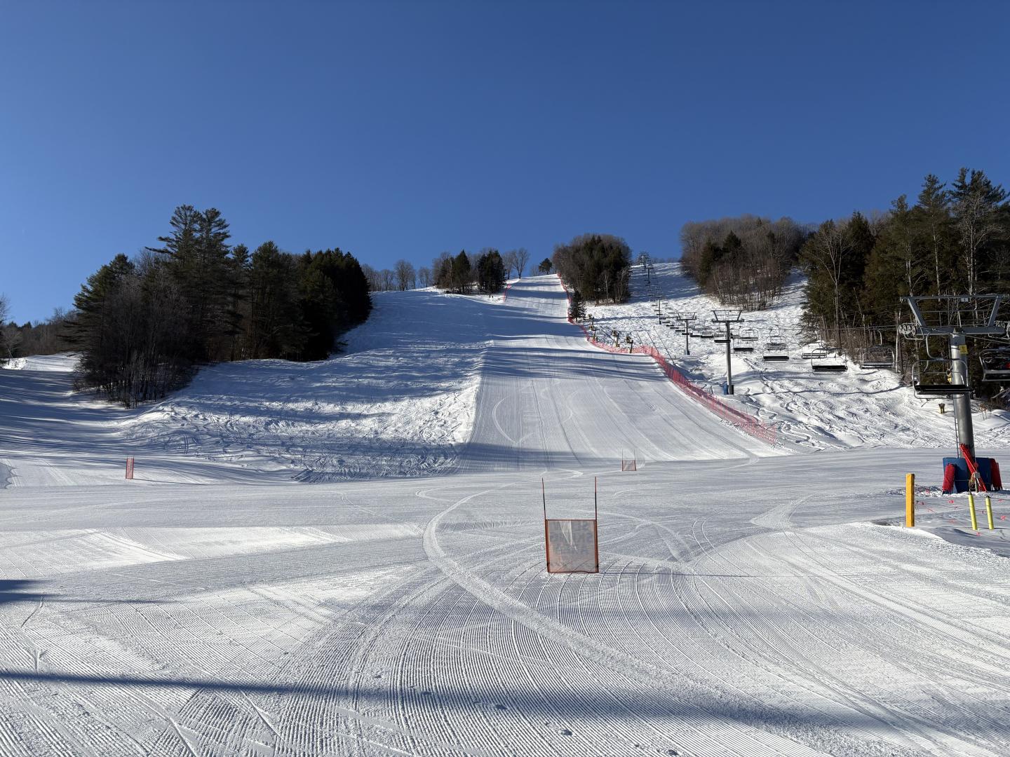 Snowy ski slope under a clear blue sky, surrounded by trees.
