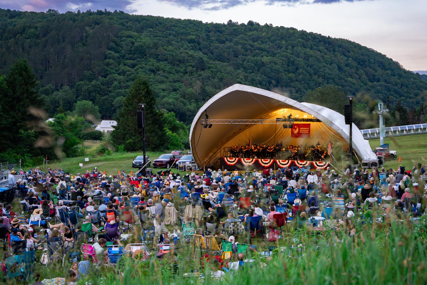 Outdoor concert with crowd, hills in the background.