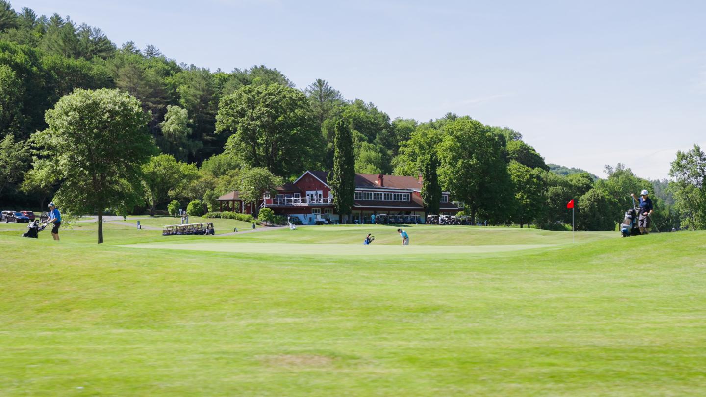 Golf course with clubhouse, surrounded by trees, under a clear sky.
